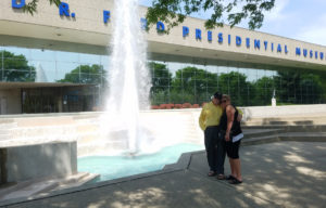 A couple smile in front of Gerald Ford museum & fountain.
